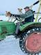 Mann auf grünem Traktor mit zwei Hunden im Schnee