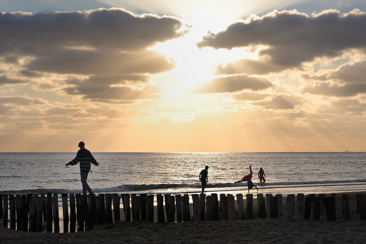 People on the beach doing beach stuff. Sunset in the background.